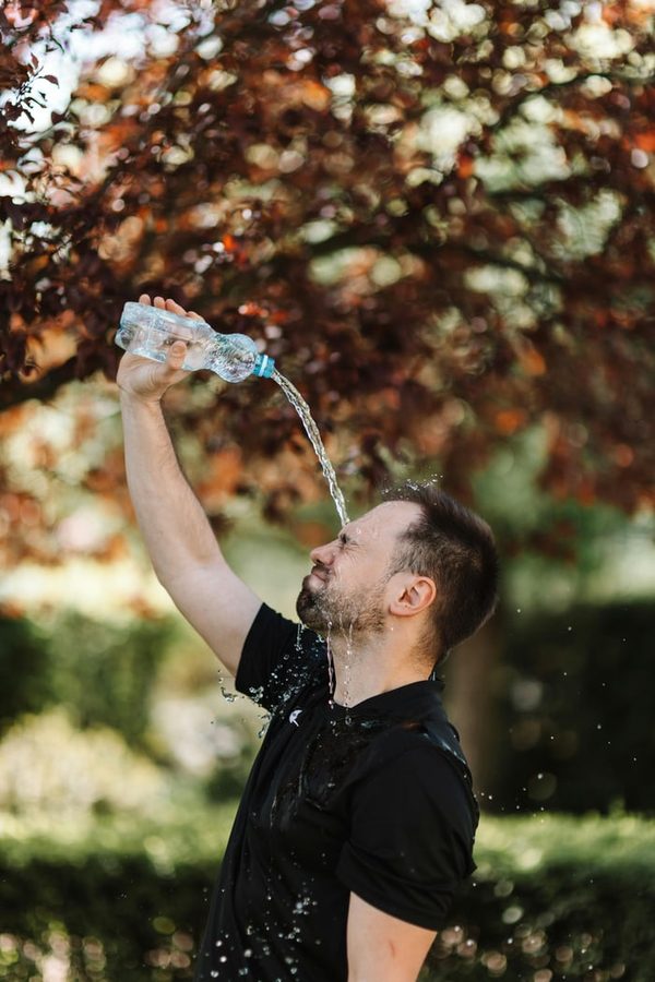 Mann gießt sich an einem heißen Tag Wasser über das Gesicht