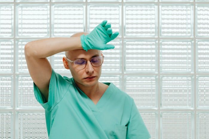Pflegekraft in Berufskleidung wischt sich bei Hitze die Stirn